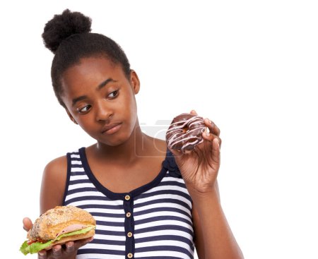Foto de Tratando de tomar una decisión saludable. una joven afroamericana tratando de elegir entre comer una dona o un sándwich - Imagen libre de derechos