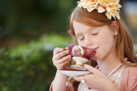 Photo for I want to be just like mummy when I grow up. A small girl playing dress up in her garden and having a pretend tea party - Royalty Free Image