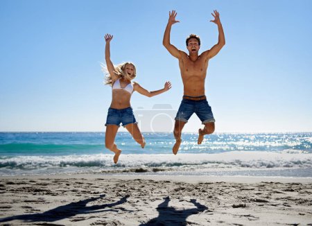 Foto de Saltando al sol. Una joven pareja saltando al aire mientras disfruta de un día en la playa - Imagen libre de derechos