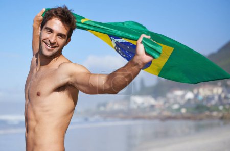 Foto de He loves his country. A handsome muscular man waving Brazilian flag on the beach - Imagen libre de derechos