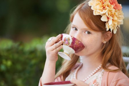 Téléchargez les photos : Sirotant mon thé... Une jeune fille jouant habiller et sirotant de sa tasse de thé dans le jardin - en image libre de droit