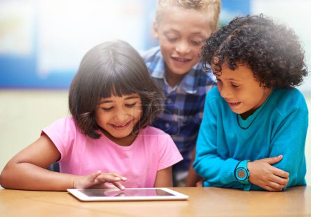 Foto de Aprender los ABC de la tecnología. niños de primaria que usan una tableta digital mientras están sentados en clase - Imagen libre de derechos