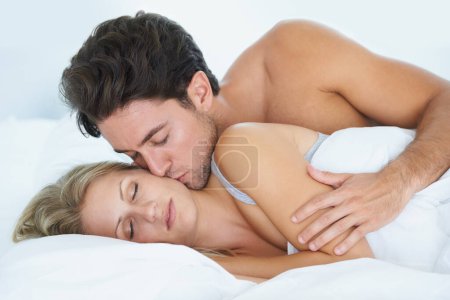 Téléchargez les photos : La réveiller de son sommeil. Un mari embrassant sa femme et l'embrassant affectueusement sur la joue pendant qu'elle dort allongée au lit - en image libre de droit