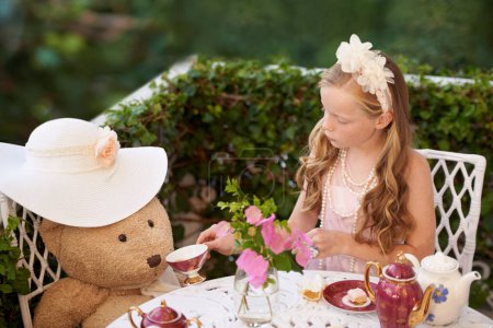 Foto de Té con Teddy. Una niña sentada afuera tomando un té con su osito de peluche - Imagen libre de derechos