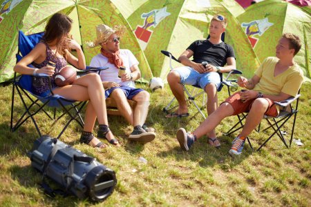 Téléchargez les photos : Passer du temps loin de la scène. Quatre amis assis devant leur tente prennent un verre et discutent - en image libre de droit