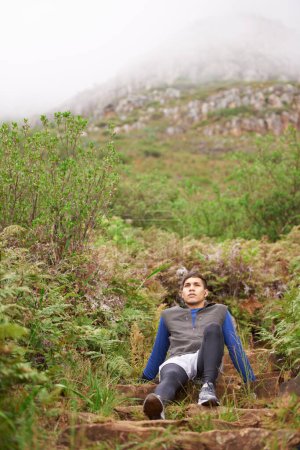 Foto de ¡Uf, qué entrenamiento! Un joven sentado en la ladera de la montaña - Imagen libre de derechos