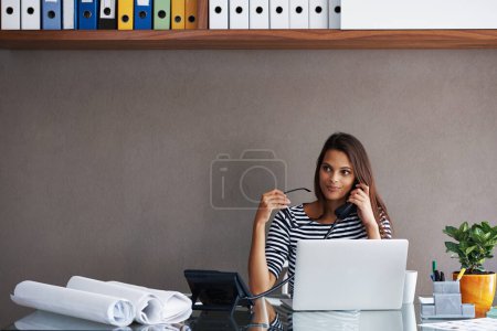 Foto de El negocio está bien. Una joven mujer de negocios al teléfono mientras está sentada en el escritorio de su oficina - Imagen libre de derechos