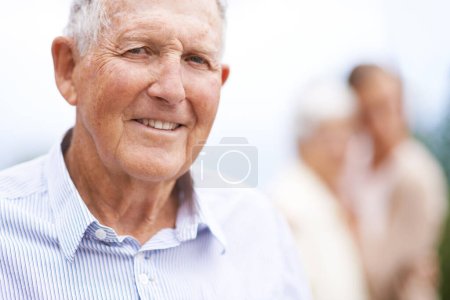 Téléchargez les photos : Vieillir... mais aussi être plus heureux. Portrait d'un homme âgé debout dehors avec des gens flous en arrière-plan - en image libre de droit