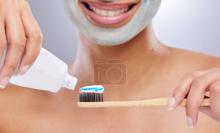 Foto de Enorgullécete de tu higiene personal. una mujer irreconocible usando una mascarilla y aplicando pasta de dientes a su cepillo de dientes en el estudio - Imagen libre de derechos