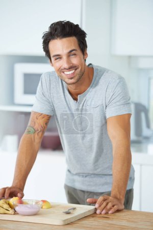Photo for Hes passionate about healthy eating. Portrait of a gorgeous young man leaning against a kitchen counter and smiling - Royalty Free Image