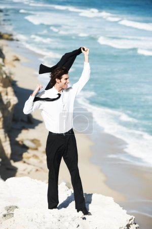 Photo for Breathing in the fresh air of freedom. Handsome businessman standing on a cliff above the ocean waving his jacket in the air - Royalty Free Image
