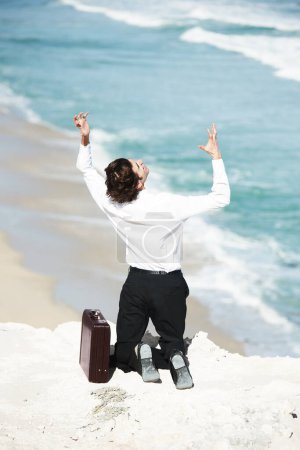 Photo for I cant do this anymore. Businessman kneeling on a cliff overlooking the ocean with his hands in the air - Royalty Free Image