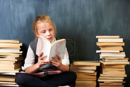Photo for Catching up on some studies. A cute blonde girl reading in class surrounded by books - Royalty Free Image