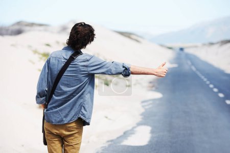 Foto de Solo yo y el camino abierto... Vista trasera de un joven de moda haciendo autostop en el lado de la carretera - Imagen libre de derechos