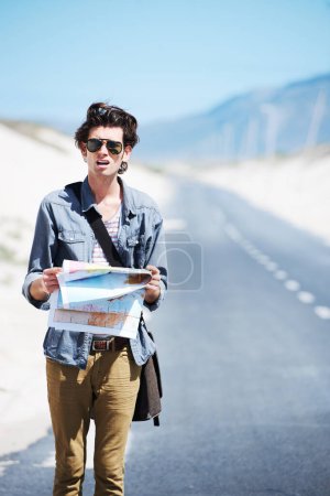 Foto de Aturdido y confundido. Joven perdido parado a un lado de la carretera sosteniendo un mapa y mirando confundido - Imagen libre de derechos