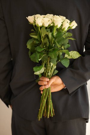 Foto de Listo para sorprender a ese alguien especial. Imagen recortada de un joven con un traje sosteniendo un ramo de rosas a sus espaldas - Imagen libre de derechos