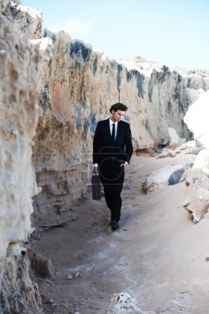 Photo for Getting back to nature. Handsome businessman strolling along the sand next to a rock formation, carrying a briefcase - Royalty Free Image