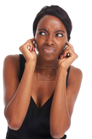 Foto de No oigo nada. Frunciendo el ceño a una joven africana con los dedos en las orejas - aislada en blanco - Imagen libre de derechos