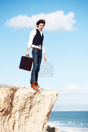 Foto de Llegar a nuevas alturas en los negocios. Joven hombre de negocios semi-formal parado en un acantilado con vistas al océano - Imagen libre de derechos