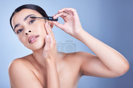 Photo for Studio portrait of a beautiful young mixed race woman with glowing skin posing against blue copyspace background. Hispanic woman with natural looking eyelash extensions applying mascara. - Royalty Free Image