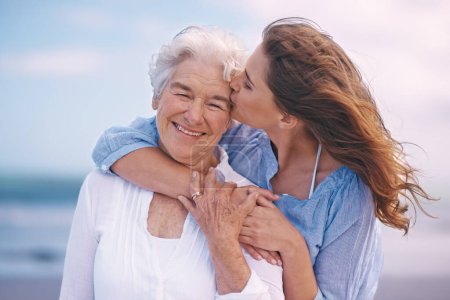 Photo for Woman, kiss and senior mother at beach with happiness, love and smile for mothers day on vacation. Elderly lady, daughter and happy with hug, bonding and outdoor by ocean for holiday in retirement. - Royalty Free Image