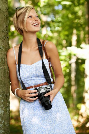 Téléchargez les photos : Profiter d'une journée de photographie en plein air. Jeune photographe mignon tenant son appareil photo et s'appuyant contre un arbre - en image libre de droit