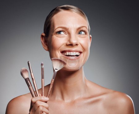 Téléchargez les photos : Belle femme mature posant avec une brosse de maquillage en studio sur un fond gris. - en image libre de droit