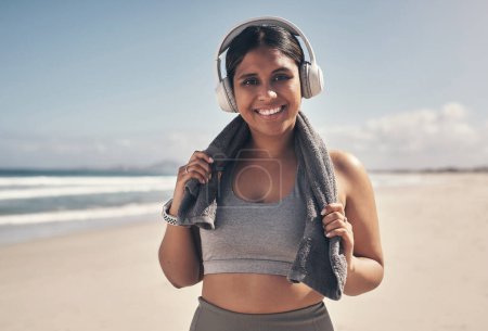 Photo for I have the best time when Im out running to the beat. a sporty young woman wearing headphones and a towel around her neck on the beach - Royalty Free Image