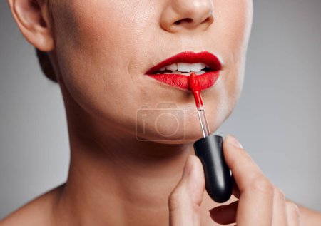 Beautiful mature woman posing with red lipstick in studio against a grey background.