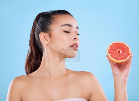 Photo for Delicious and full of goodness. Studio shot of an attractive young woman posing with half a grapefruit against a blue background - Royalty Free Image