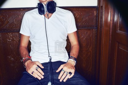Foto de Tomando un descanso de la música. un joven con estilo sentado en un pasillo y con auriculares alrededor del cuello - Imagen libre de derechos