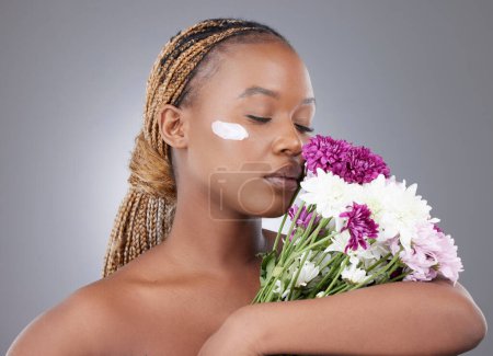 Photo for All the memories of everything youve ever smelled. Studio shot of an attractive young woman applying moisturiser while posing with flowers against a grey background - Royalty Free Image