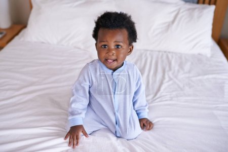 Photo for Black baby boy with tongue out in bedroom, sitting on the bed with early childhood development. African male toddler, cute curious child with growth and learning, childcare and relax at family home. - Royalty Free Image