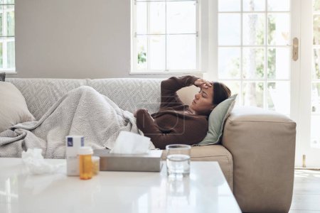 Foto de Mi temperatura no ha bajado. una joven tumbada en un sofá mientras se siente enferma en casa - Imagen libre de derechos