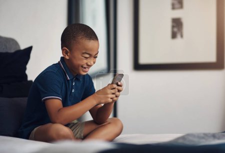 Foto de Mamá me dio su viejo celular para jugar. un niño usando un celular mientras está sentado en su cama - Imagen libre de derechos