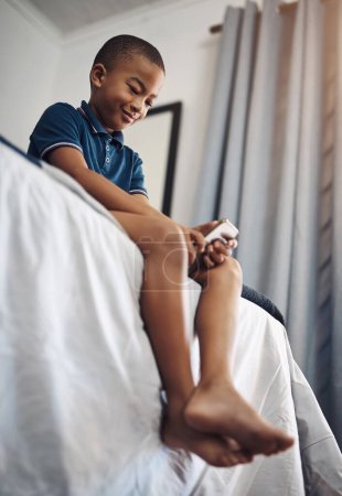 Foto de Nunca me aburriré con todos estos juegos en línea. un niño usando un celular mientras está sentado en su cama - Imagen libre de derechos