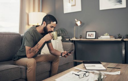 Photo for Tracking his spending with smart apps. a young man having coffee and using a smartphone while going through paperwork at home - Royalty Free Image
