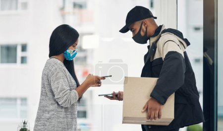 Photo for It just makes smarter sense to pay the contactless way. a masked young man and woman using smartphones during a home delivery - Royalty Free Image
