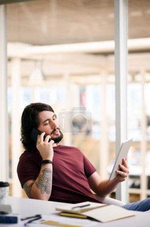 Photo for Im going to send you the updates right now. a young businessman talking on a cellphone while using a digital tablet in an office - Royalty Free Image
