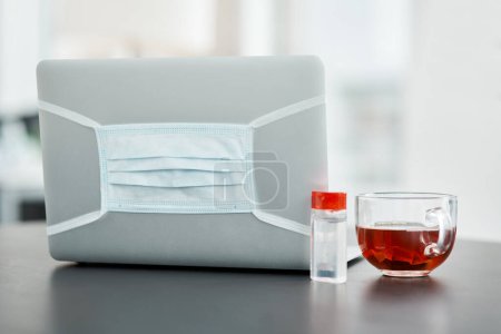 Photo for Essentials for a safe work station. a laptop, mask, hand sanitiser and herbal tea on a desk in a modern office - Royalty Free Image