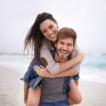 Couple, portrait and piggyback hug at beach for travel, romance and freedom together outdoors. Face, smile and happy woman embracing man on trip, vacation or holiday, bond and having fun in Florida.