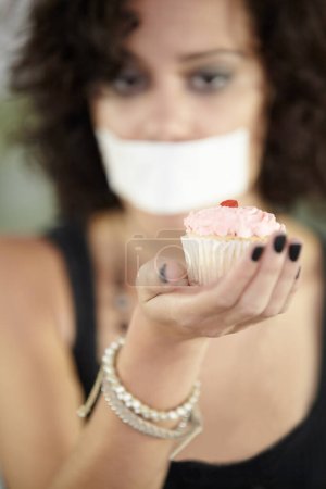 Photo for Cupcake in hand, eating disorder and a woman on diet and tape over mouth to stop or lose weight. Face, covering and restriction of female suffering with anorexia, body dysmorphia or bulimia problem. - Royalty Free Image