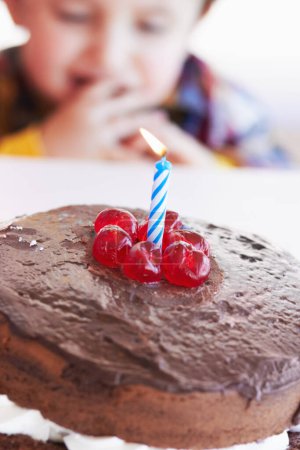 Photo for Birthday cake closeup, young kid and celebration candle with dessert at home with a child. Chocolate, cherry and candles to celebrate a boy at a party with sweets on a kitchen table in a house. - Royalty Free Image