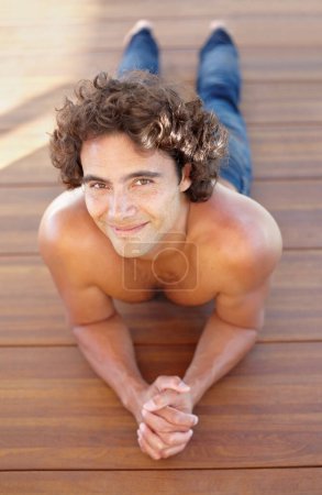 Photo for Portrait, topless and a man lying on a wooden deck outdoor in summer to relax or rest during the day. Sexy, shirtless and hot with a handsome young male person resting on a wood floor from above. - Royalty Free Image