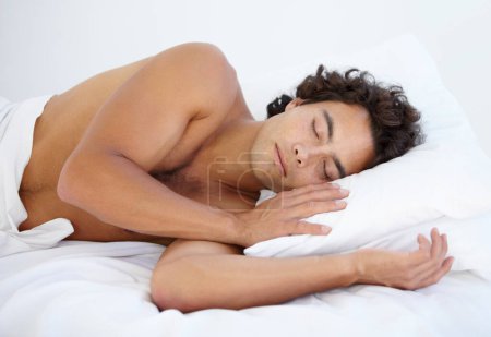 Téléchargez les photos : Repos, calme et homme dormant au lit un week-end le matin avec un oreiller moelleux à sa maison. Détendez-vous, personne paisible et masculine faisant une sieste et rêvant dans la chambre de sa maison ou de son appartement - en image libre de droit