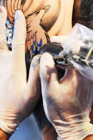 Foto de Manos, brazo y pistola de tatuaje de artista con tinta de color azul para la ilustración permanente de aves o herramienta de precisión. Primer plano del diseñador gráfico aplicando detalle a los brazos para el arte corporal, colorear o dibujar. - Imagen libre de derechos