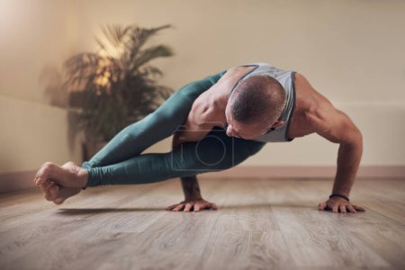 Téléchargez les photos : Le yoga est une forme de renforcement musculaire. Plan complet d'un beau jeune homme tenant une pose à huit angles pendant une séance de yoga en intérieur seul - en image libre de droit