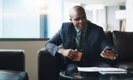 Foto de Es el hombre más ocupado del edificio. un hombre de negocios usando su celular mientras está sentado en una oficina moderna - Imagen libre de derechos