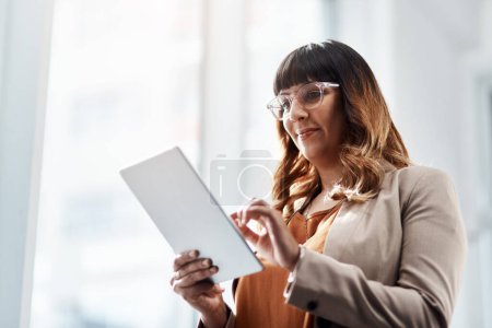 Foto de Encontrar un nicho en línea. una atractiva joven empresaria usando una tableta digital en su oficina - Imagen libre de derechos