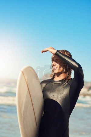 Foto de Creo que veo una gran ola entrando. un joven guapo en la playa con su tabla de surf - Imagen libre de derechos